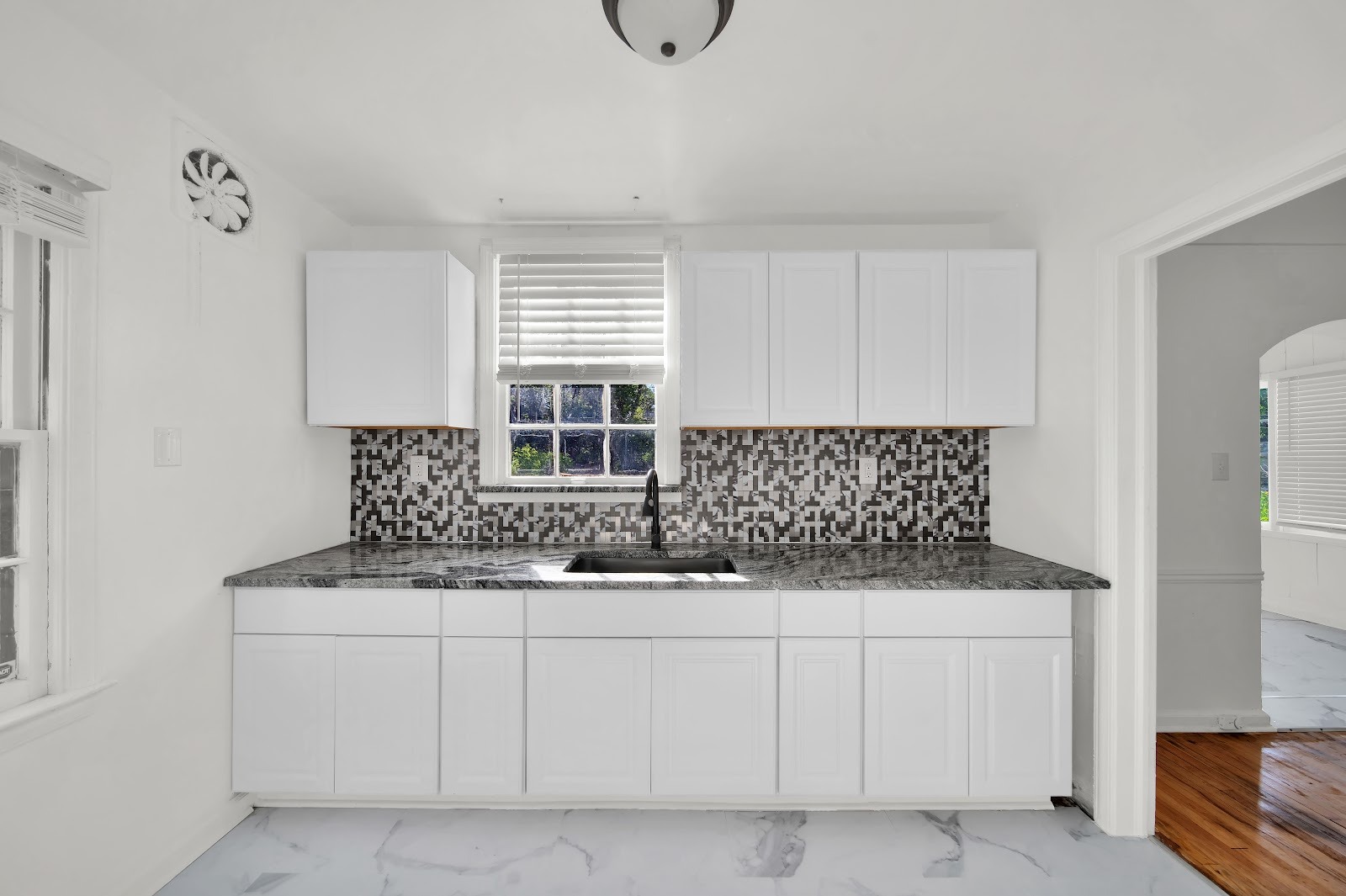 A completed white kitchen with marble-look countertops, black appliances and a patterned backsplash.