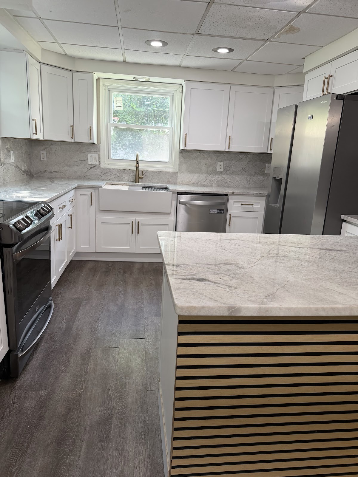 A completed white kitchen with a dark patterned backsplash, stainless appliances and a light countertop.