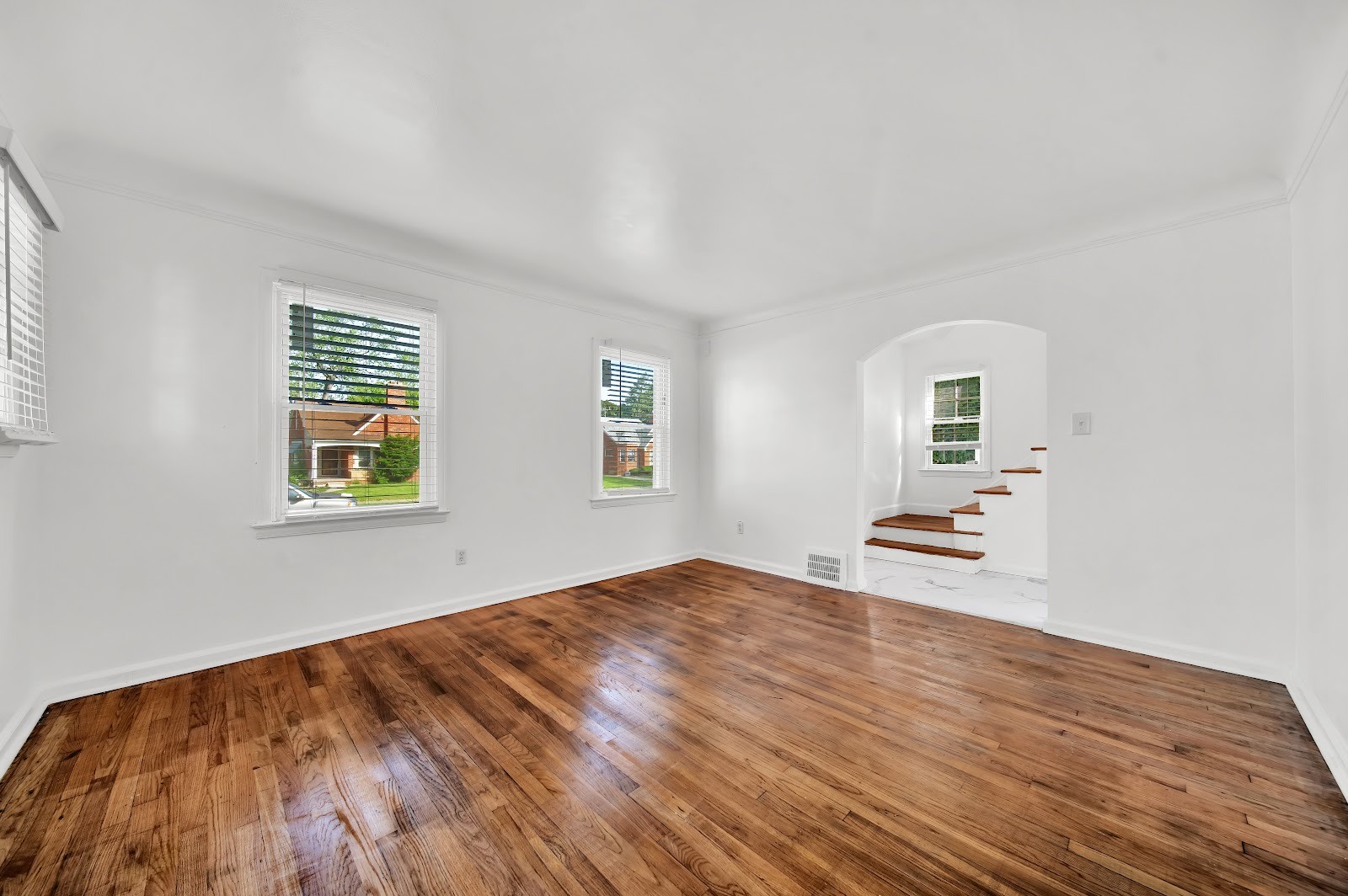 A bright finished room with polished wood floors, white walls, three windows and an arched doorway.